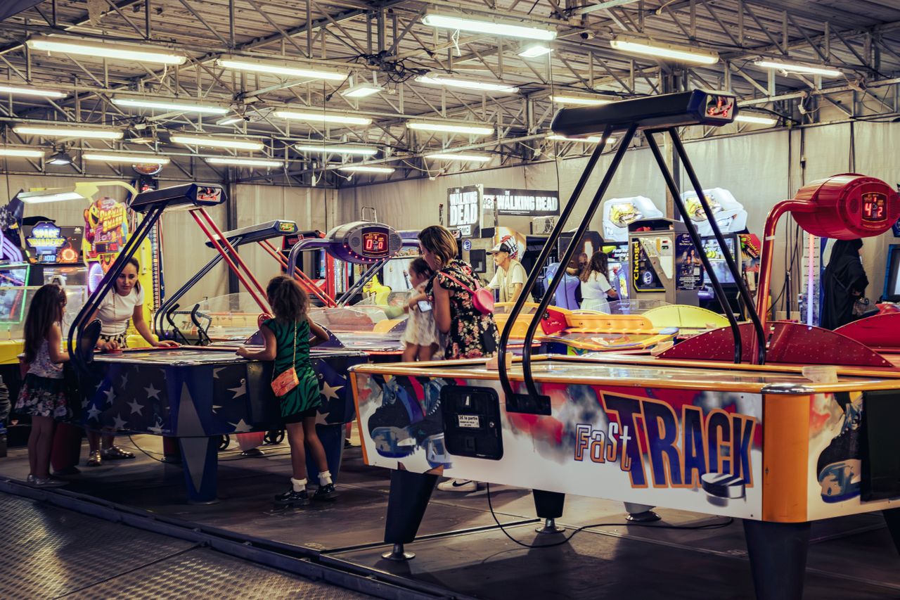 about-us-01 Children and adults enjoy air hockey games in a lively indoor arcade setting.