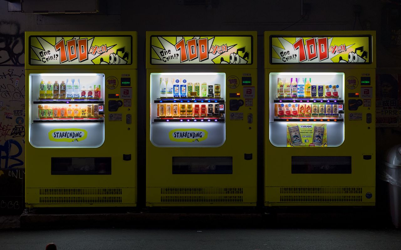 Three brightly lit vending machines on an urban street in Osaka, Japan at night.