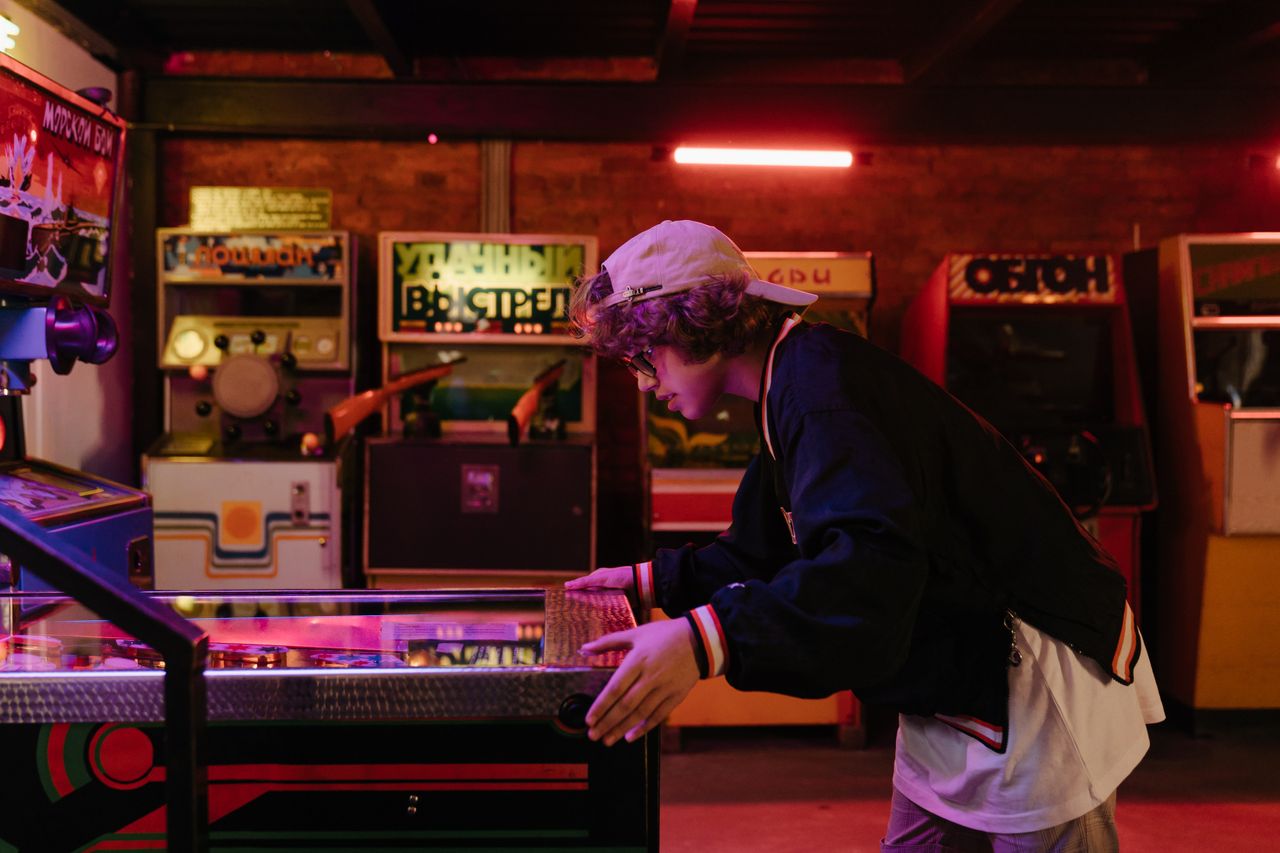 services-01 Teenager joyfully playing pinball in a nostalgic retro arcade setting.